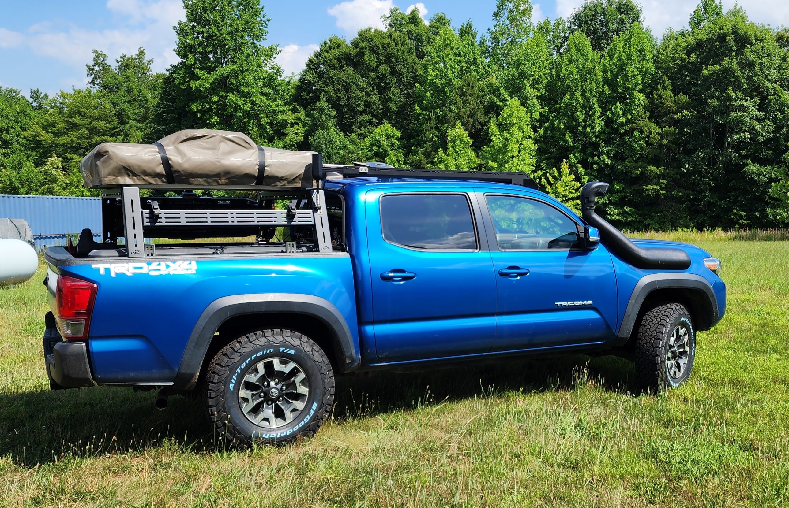 A blue Toyota Tacoma truck with a black bed rack installed on it, parked outdoors.