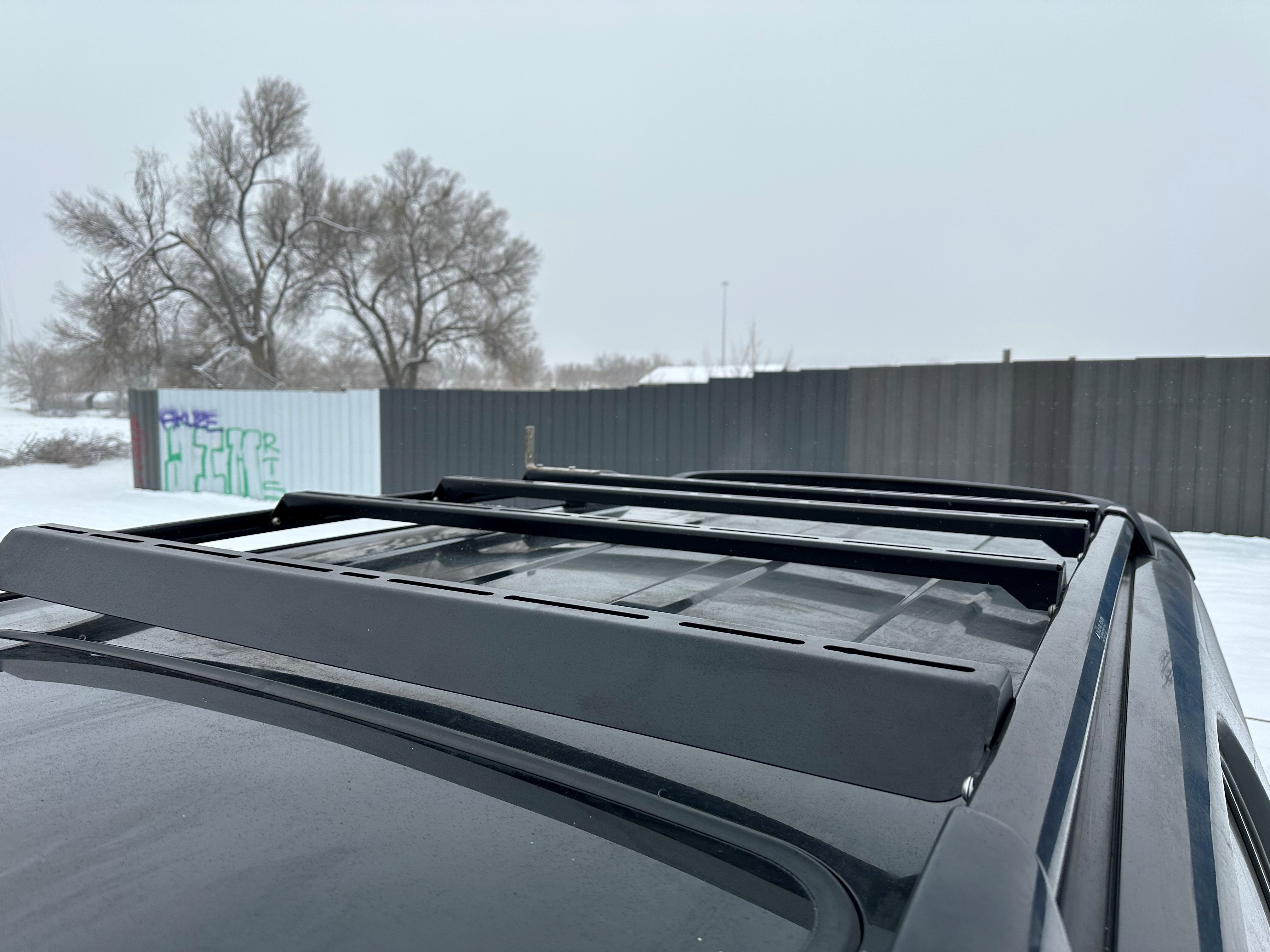 A black integrated wind fairing ruggedized crossbar on top of a vehicle, designed for use with factory side rails.