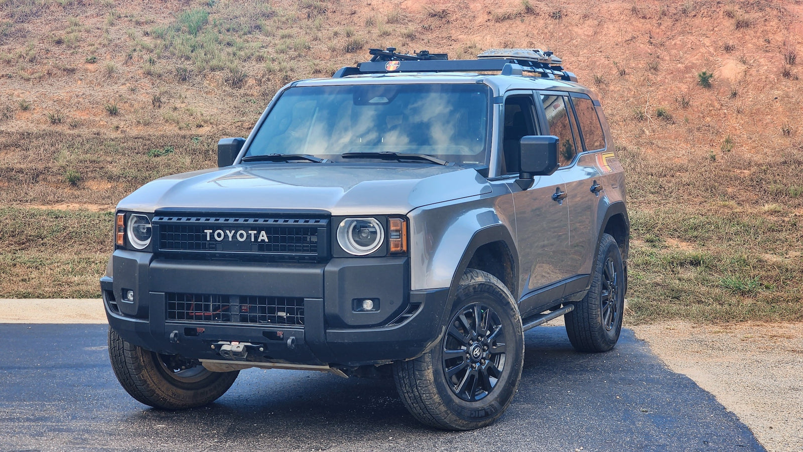 Gray Toyota Land Cruiser equipped with LFD crossbars carrying recovery boards and tools on a dirt trail.