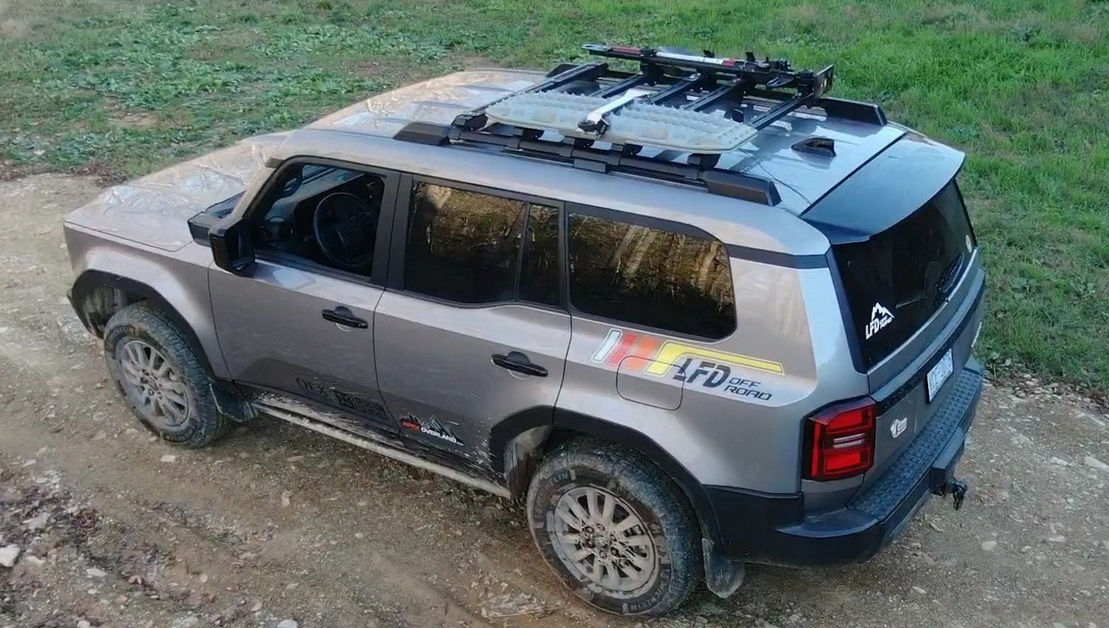 Gray Toyota Land Cruiser equipped with LFD crossbars carrying recovery boards and tools on a dirt trail.