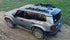 Gray Toyota Land Cruiser equipped with LFD crossbars carrying recovery boards and tools on a dirt trail.