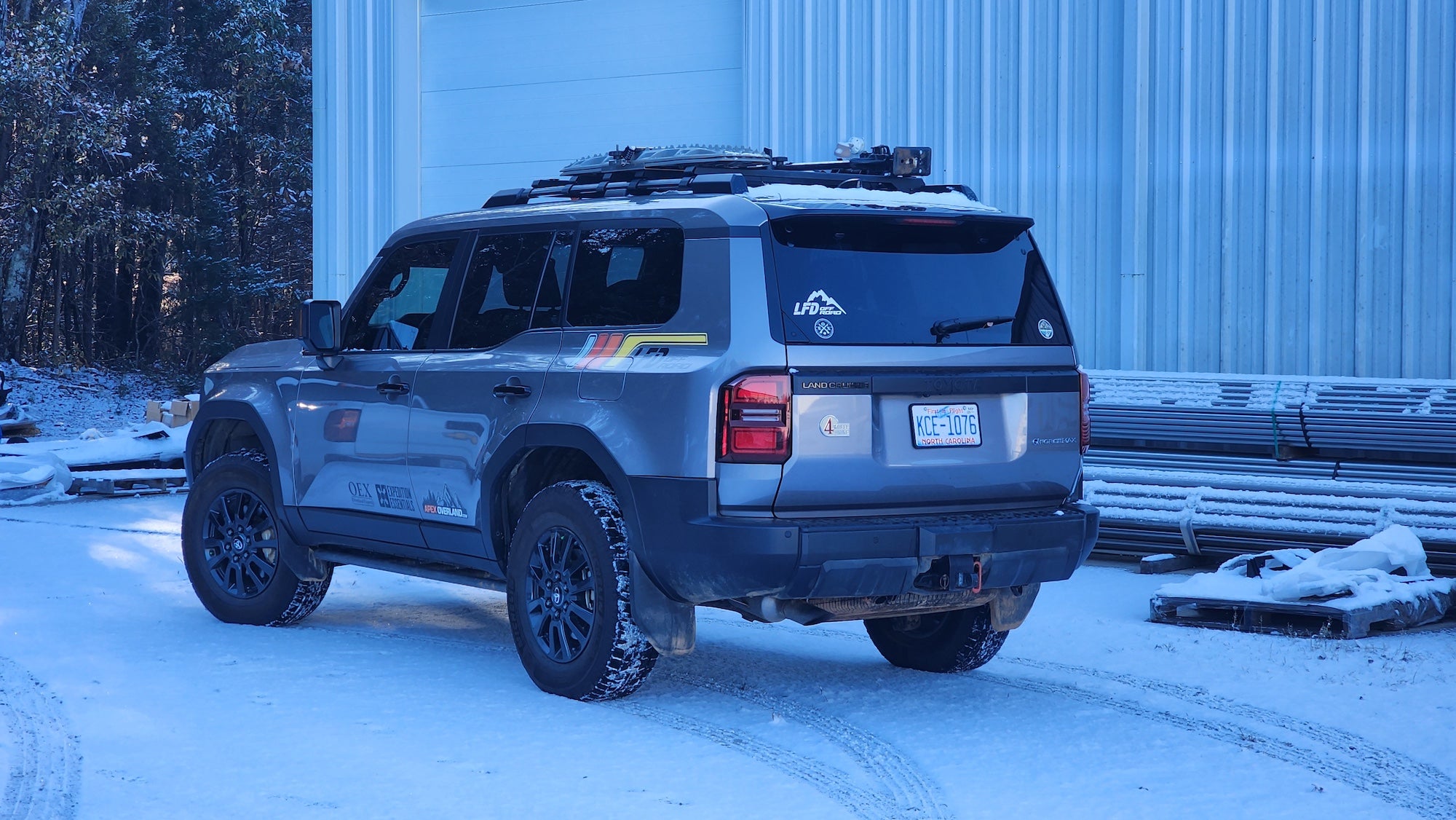 Gray Toyota Land Cruiser equipped with LFD crossbars carrying recovery boards and tools on a snowy road.