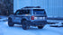 Gray Toyota Land Cruiser equipped with LFD crossbars carrying recovery boards and tools on a snowy road.