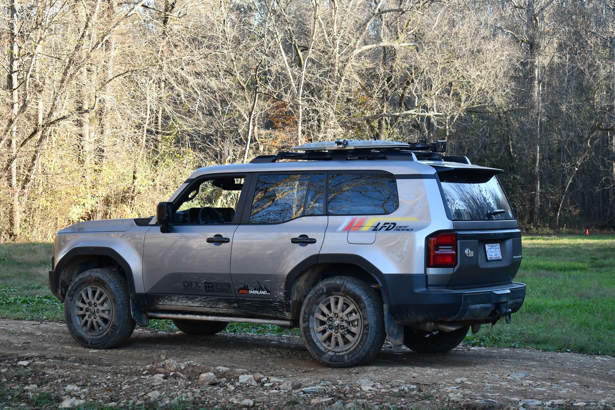 Gray Toyota Land Cruiser equipped with LFD crossbars carrying recovery boards and tools on a dirt trail.