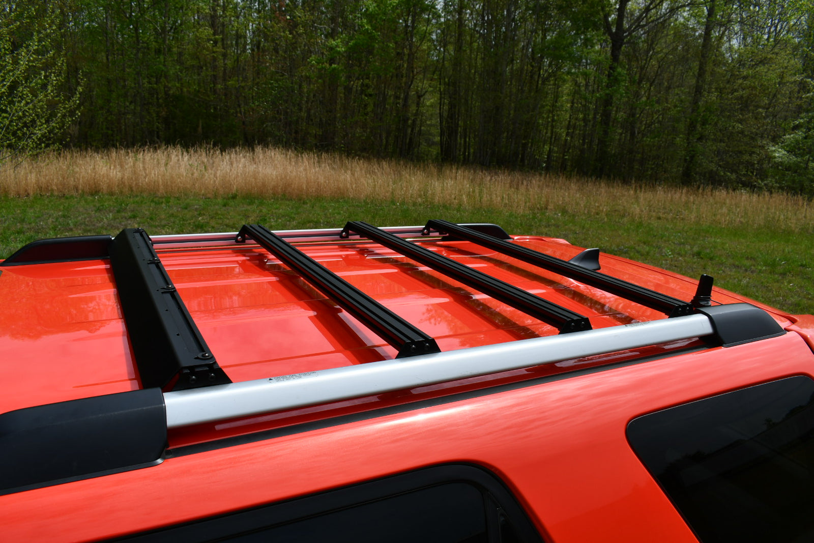 Ruggedized Aluminum Extrusion Crossbars mounted on the roof of an orange 4Runner SUV.