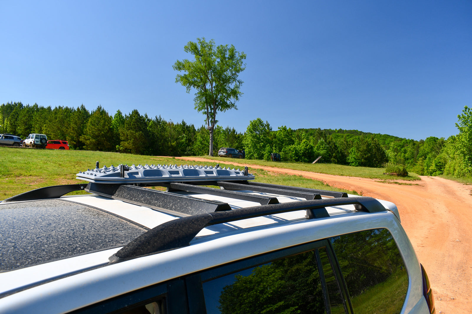 Ruggedized Crossbars mounted on the roof of a GX470 with a clear sky and trees in the background.