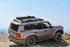 A silver 2024+ Land Cruiser with a black full length roof rack installed on top.