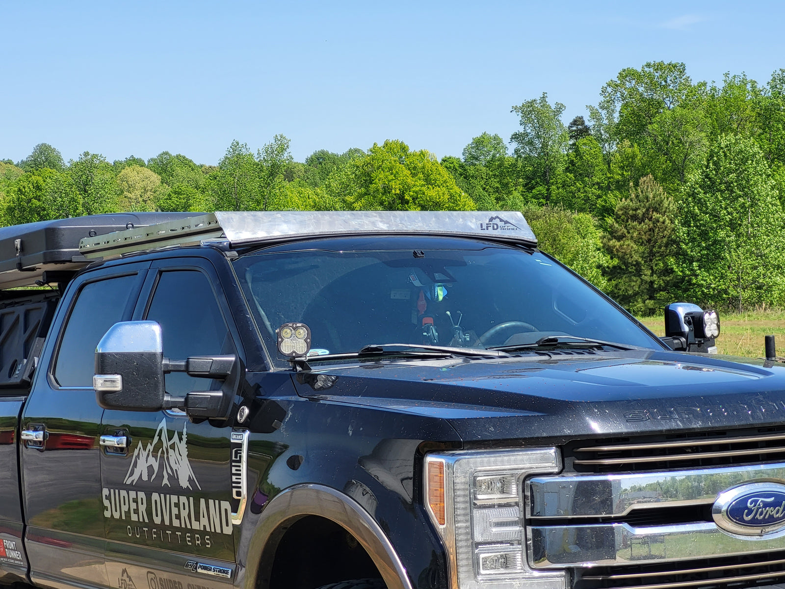 A black Ford F-Series Crewmax Cab truck with a roof rack installed on top. The rack has multiple crossbars and is made of steel with a black powder coat finish.