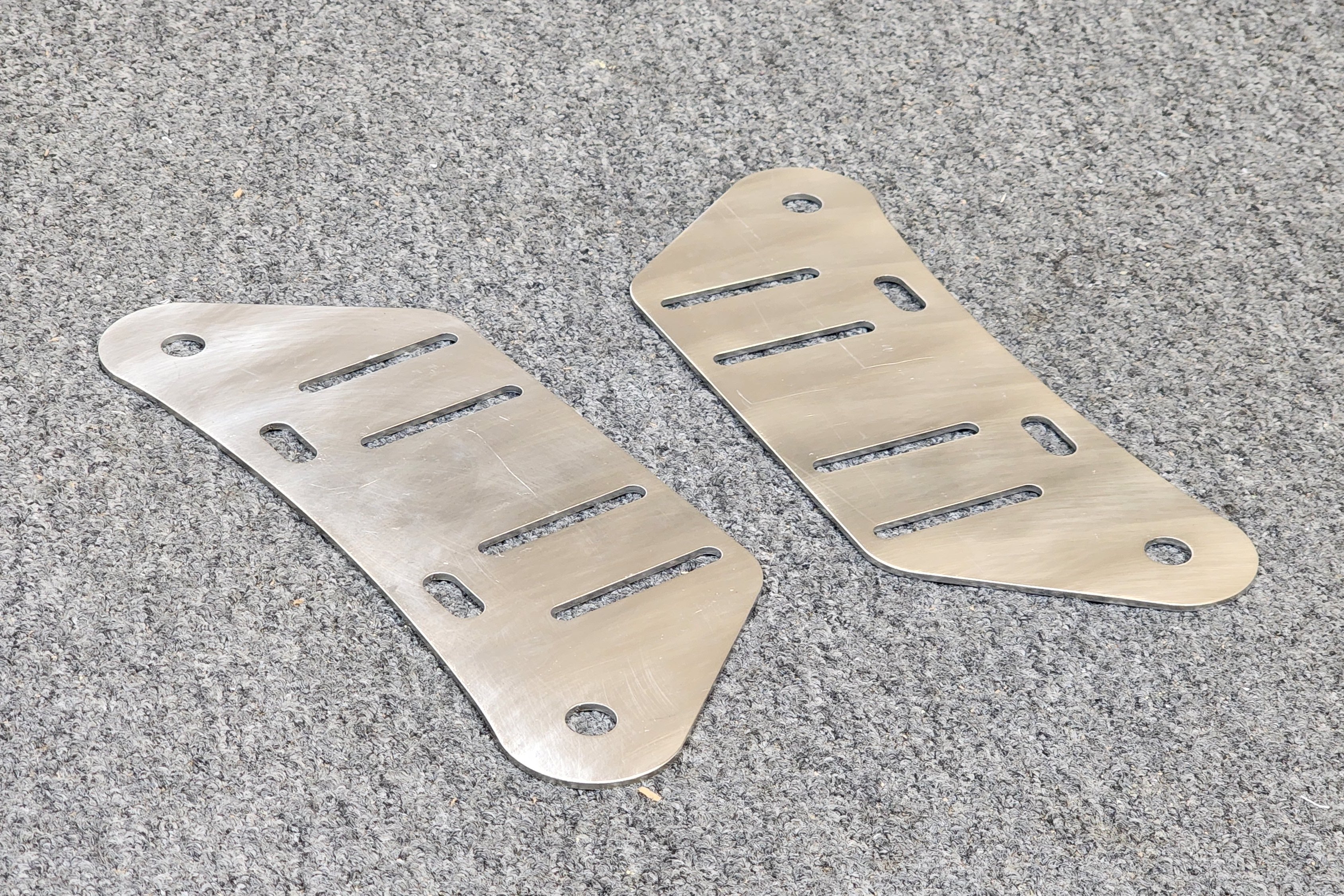 Two stainless steel traction board pin adapter plates laid on a grey surface.