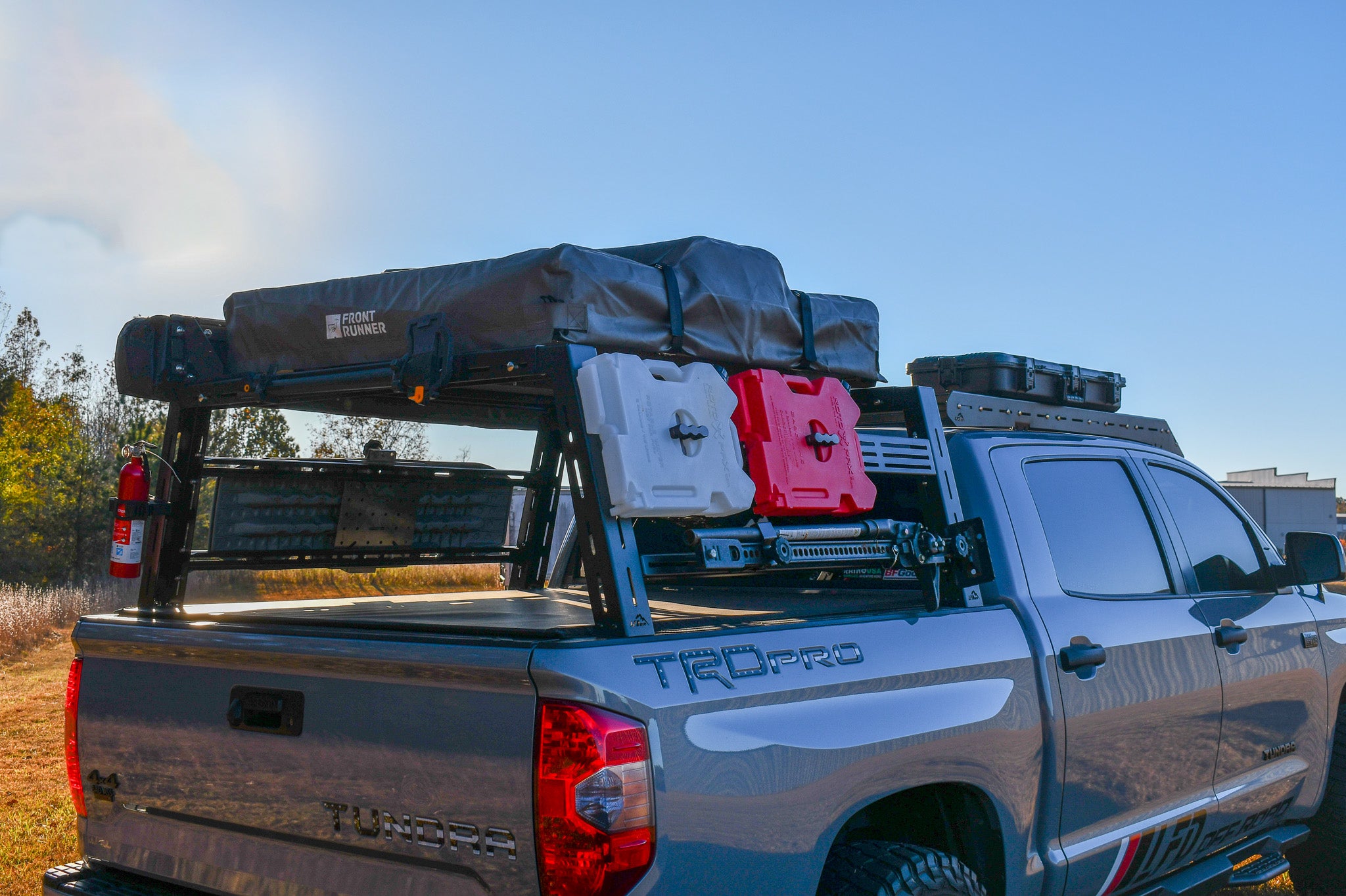 A close-up of a black steel bed rack system installed on the bed of a gray truck, featuring various modular crossbars designed for carrying gear.