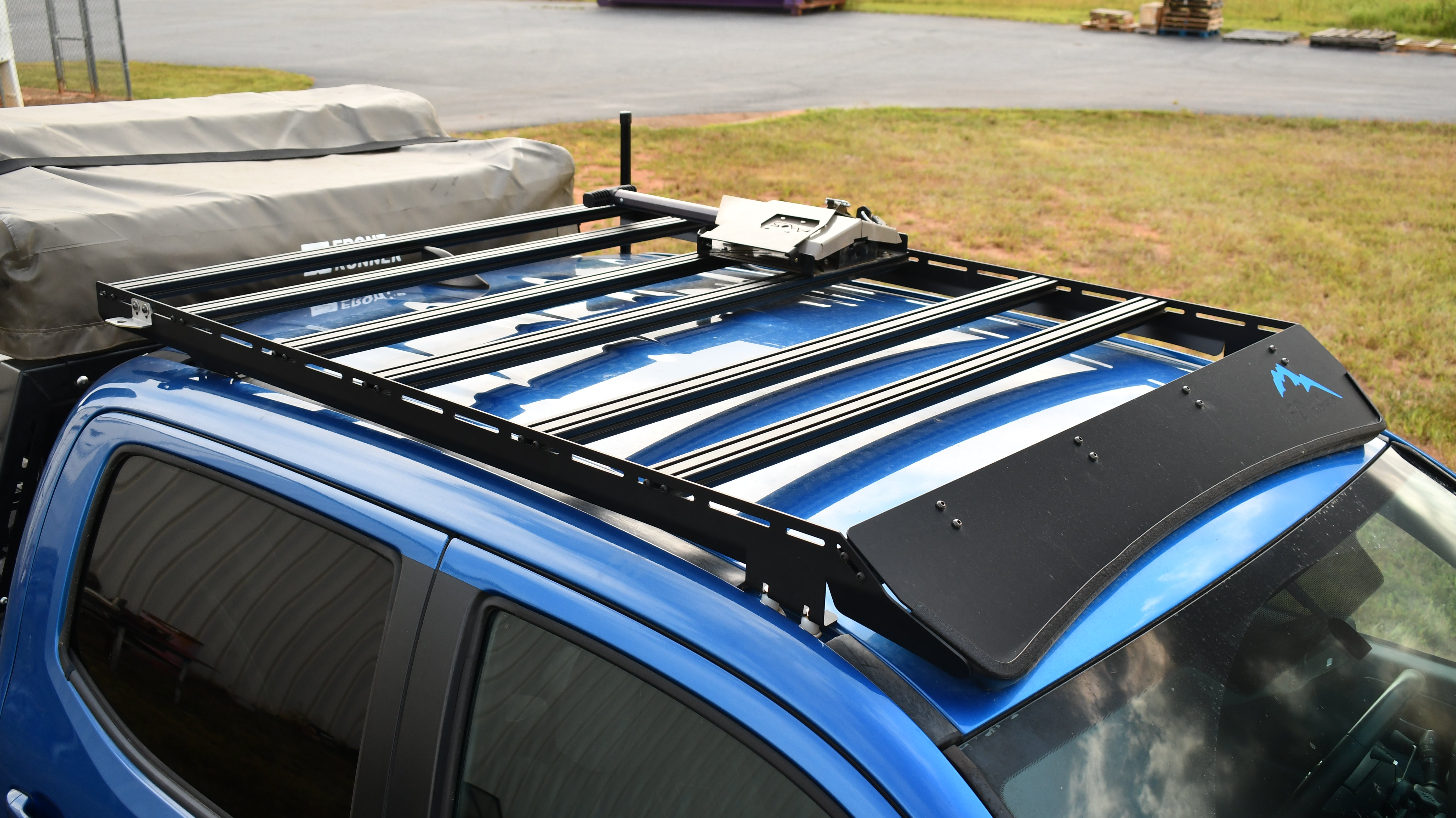 A black low profile aluminum extrusion rack mounted on top of a blue vehicle.