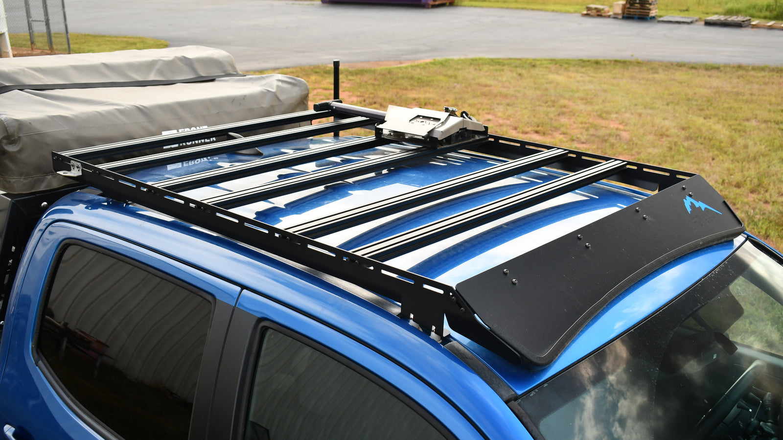 A black low profile aluminum extrusion rack mounted on top of a blue vehicle.