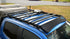 A black low profile aluminum extrusion rack mounted on top of a blue vehicle.
