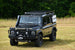 A black Ineos Grenadier SUV with a roof rack installed, set against a natural background.