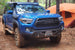 A blue Toyota Tacoma with a custom hybrid front bumper designed for 3rd Gen Tacoma models (2016-2023).