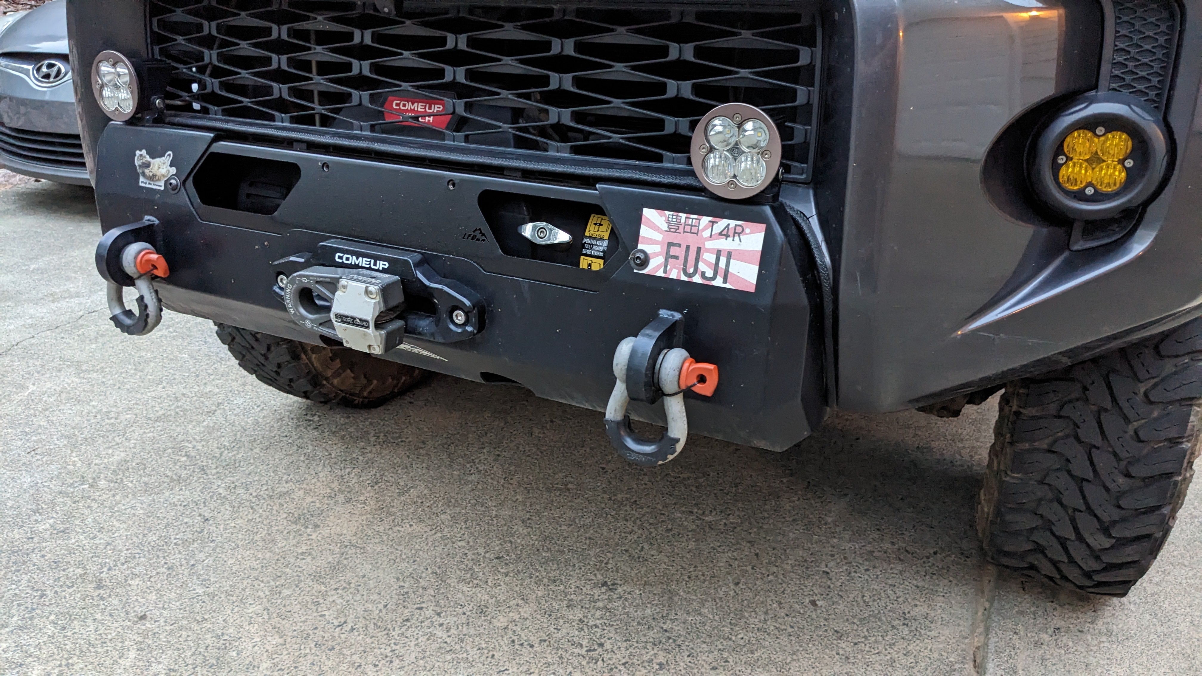 A black hybrid front bumper installed on a Lexus GX460 SUV, featuring recovery points and a winch mount.