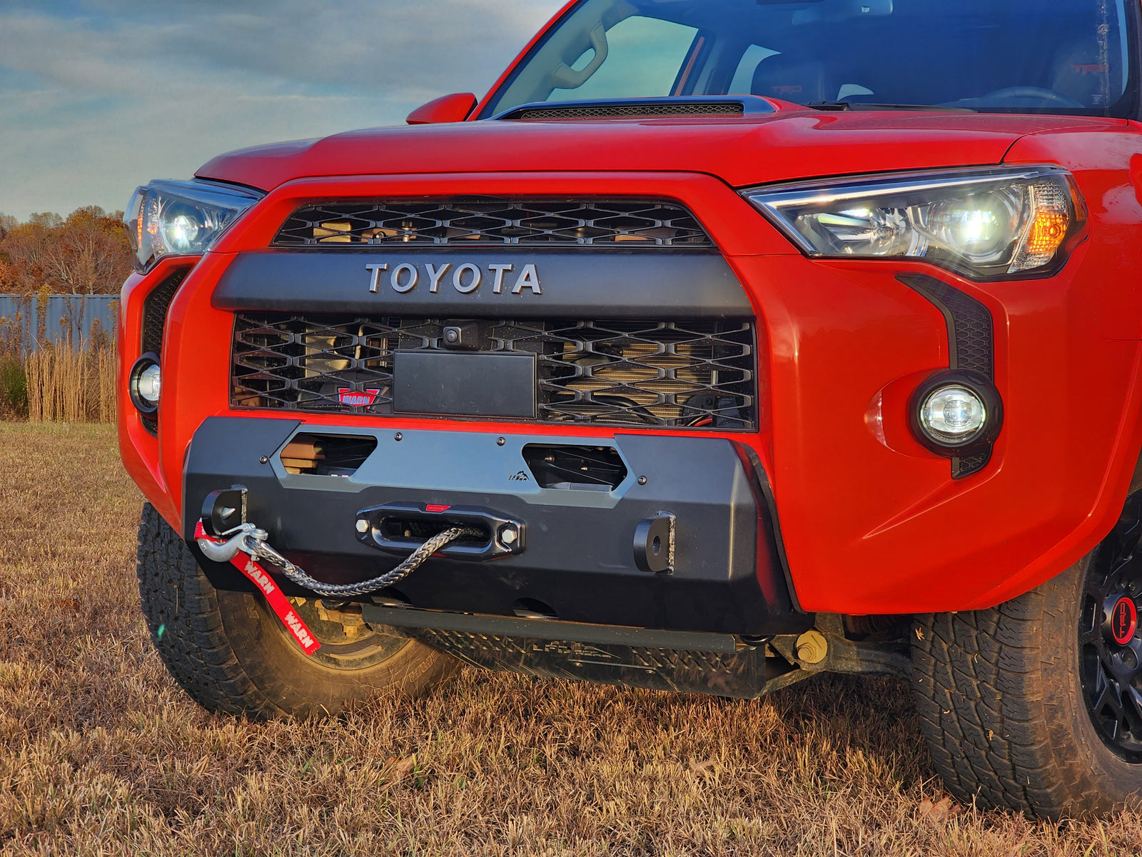 A black hybrid front bumper designed for a 5th Gen 4Runner, featuring a winch mount and recovery points, installed on a red Toyota 4Runner.