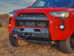 A black hybrid front bumper designed for a 5th Gen 4Runner, featuring a winch mount and recovery points, installed on a red Toyota 4Runner.
