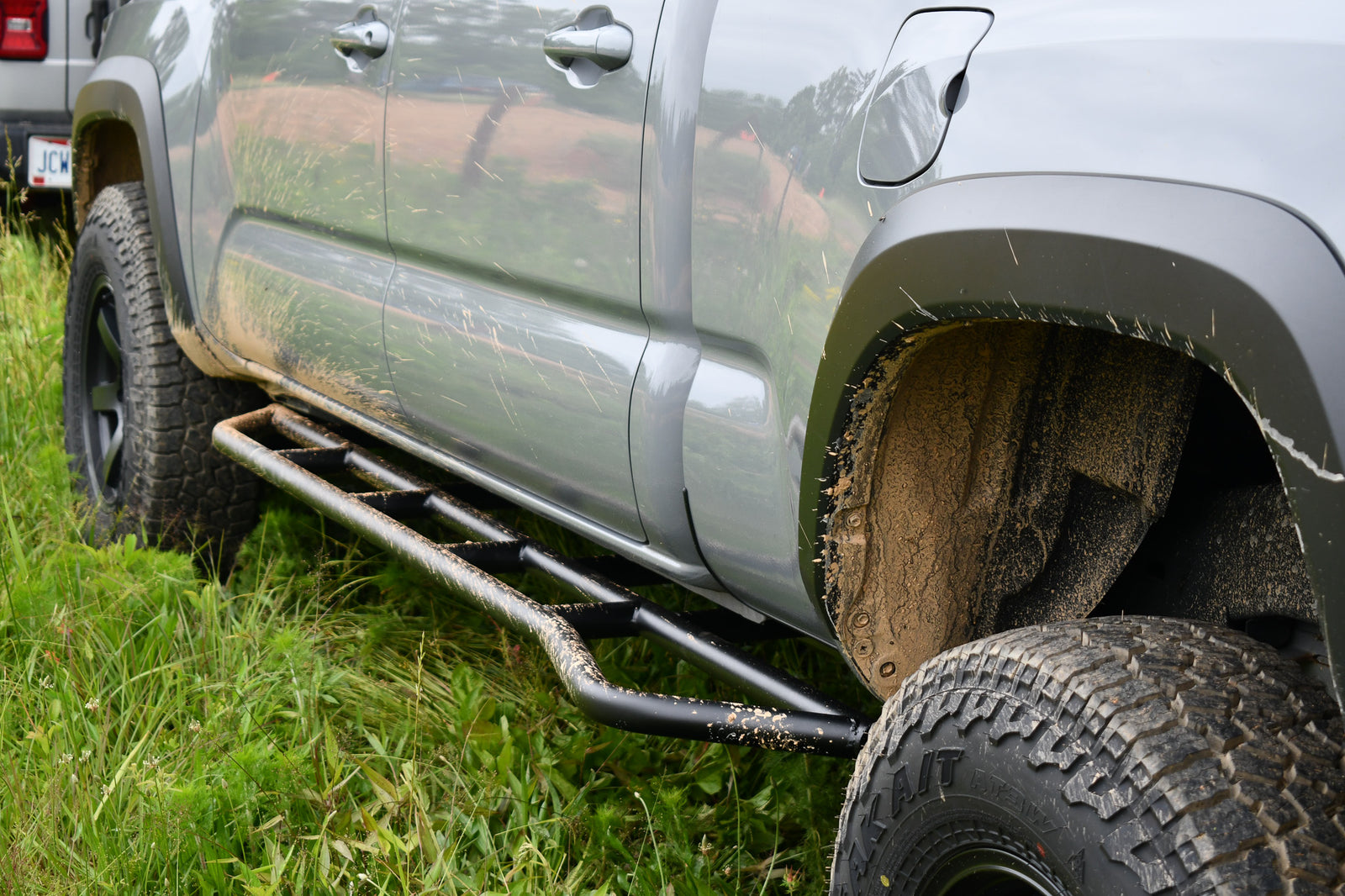 Black metal rock sliders installed on the lower front side of a gray truck, designed to protect the vehicle's rocker panels.