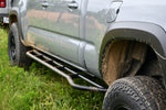 Black metal rock sliders installed on the lower front side of a gray truck, designed to protect the vehicle's rocker panels.