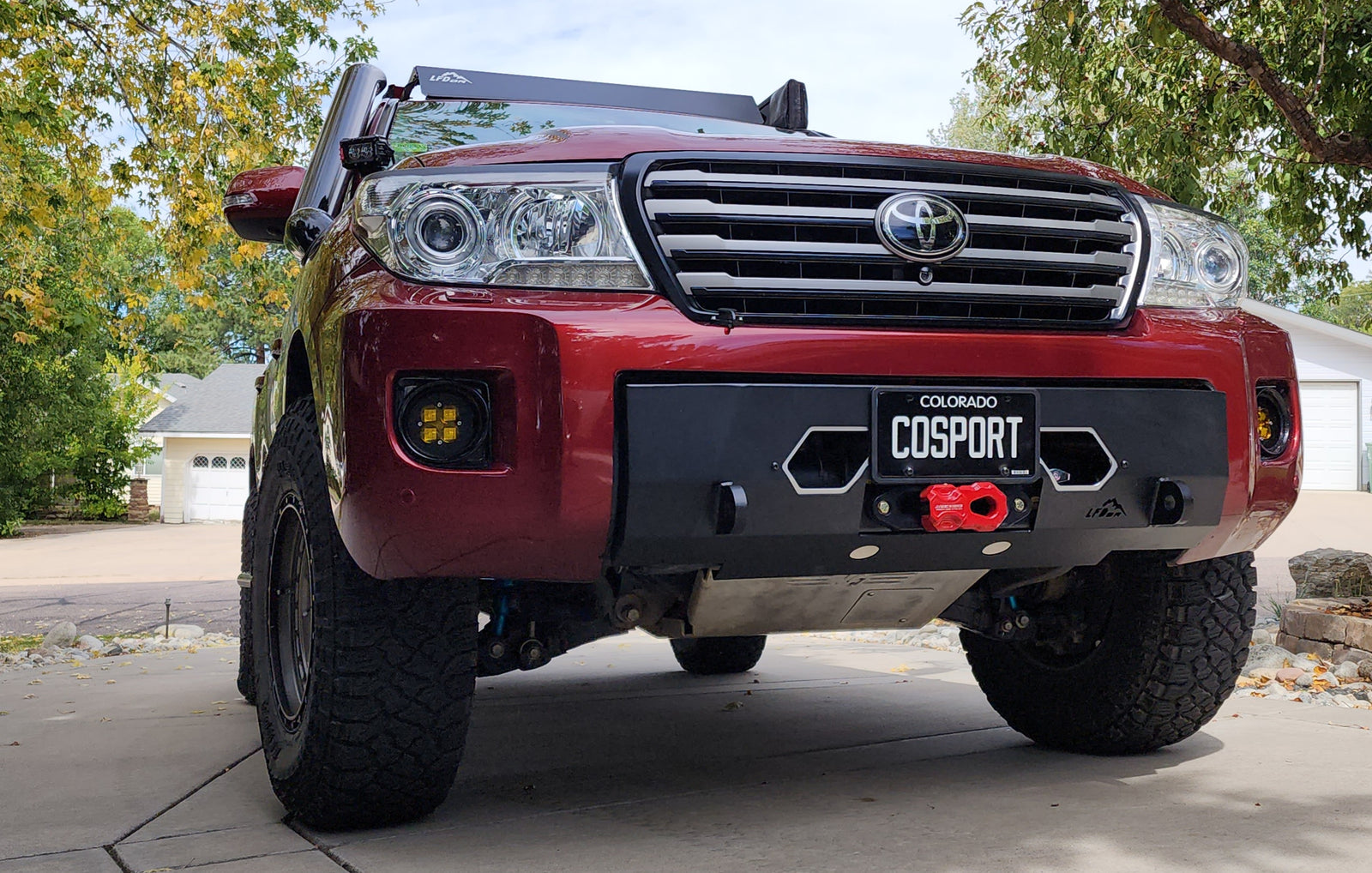 Front bumper for Land Cruiser 200 featuring a winch mount, recovery points, and lower grille, displayed on a red vehicle.