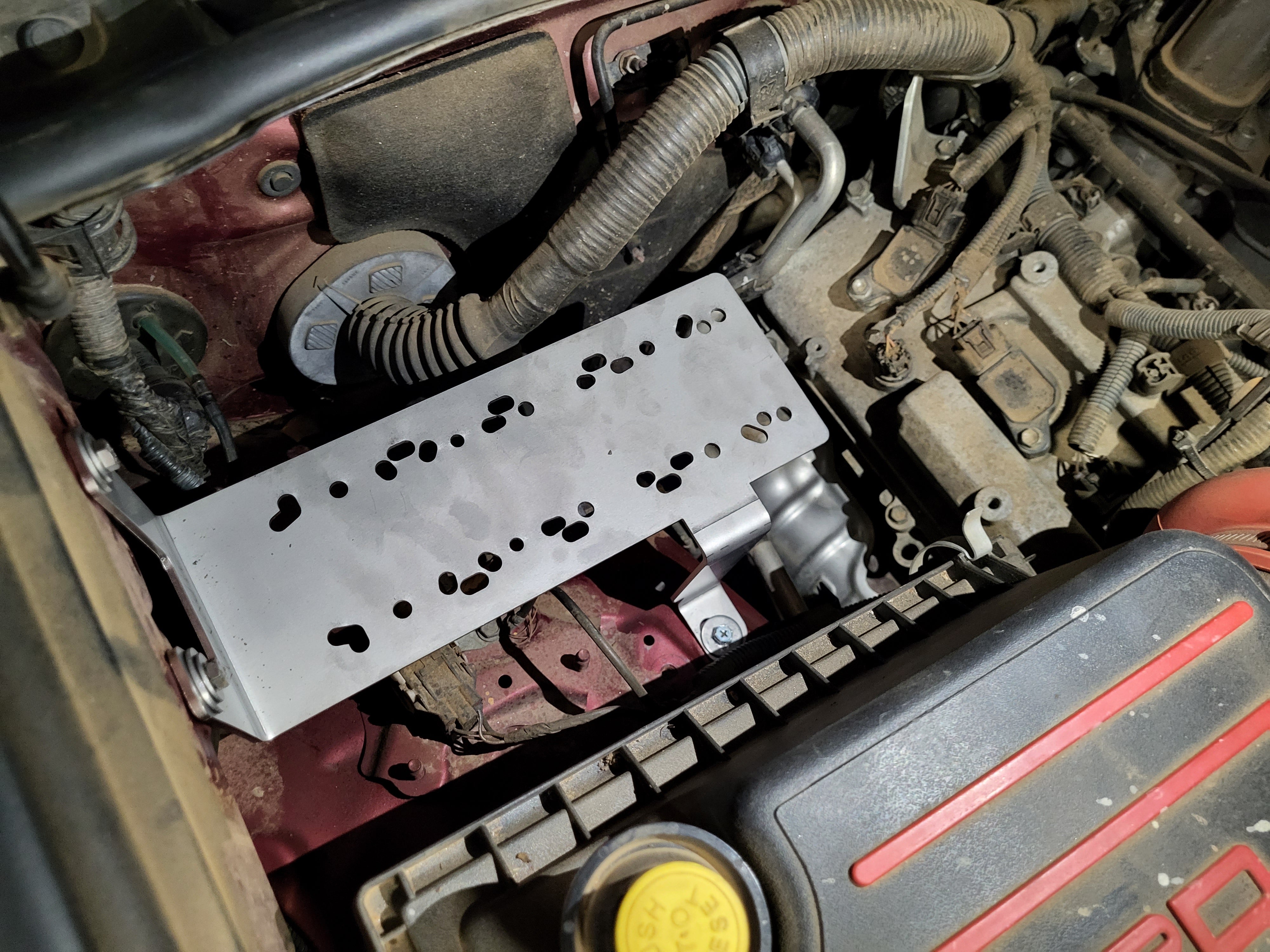 Stainless steel air compressor mount installed in the engine bay of a vehicle.