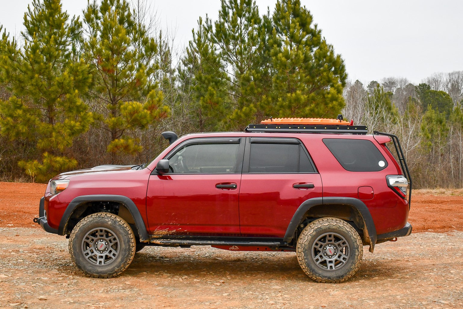 A red 5th Gen 4Runner with a 3/4 roof rack installed on top, situated in a natural setting with trees in the background.