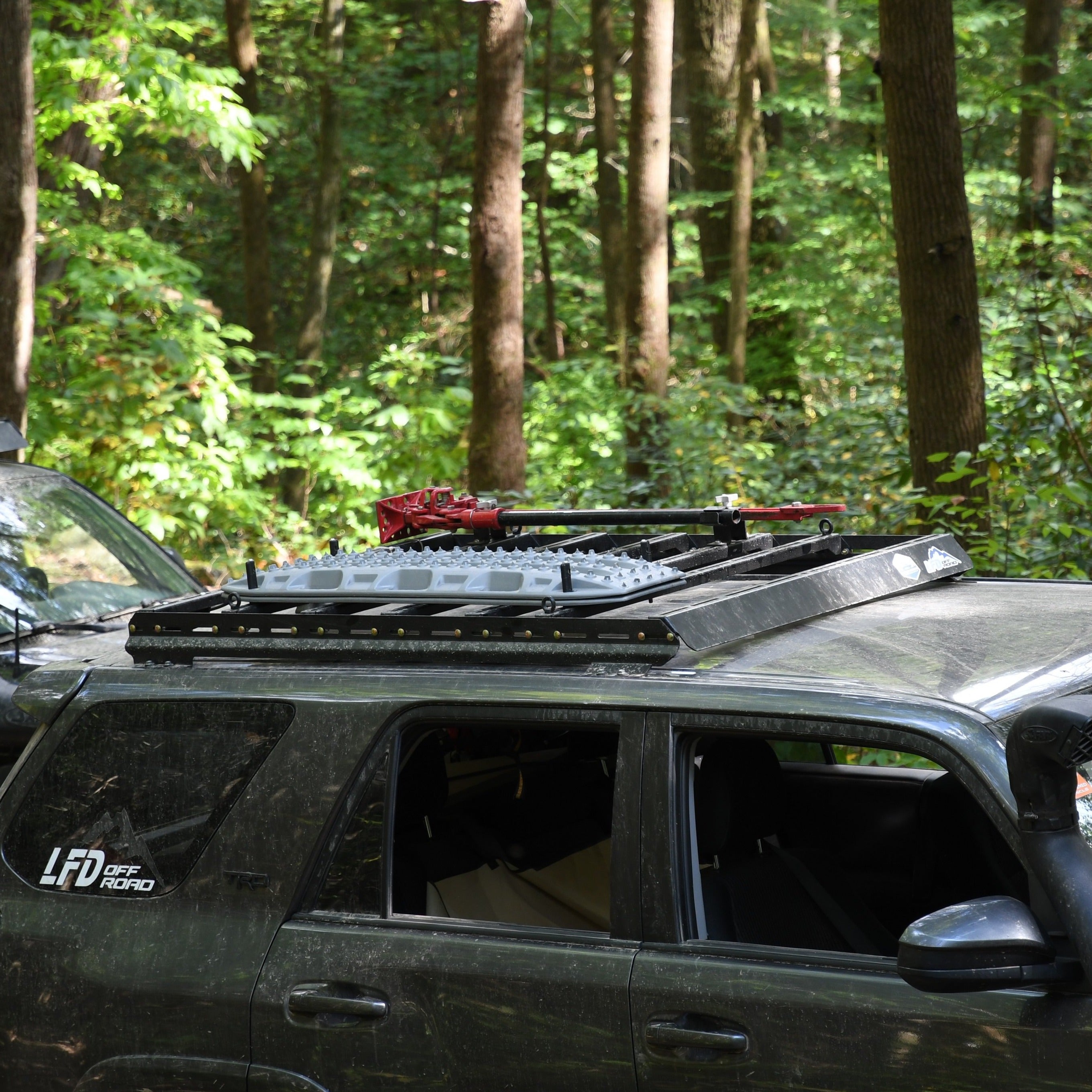 A roof rack side rail and fairing mounted on the roof of a vehicle, with a forest background.
