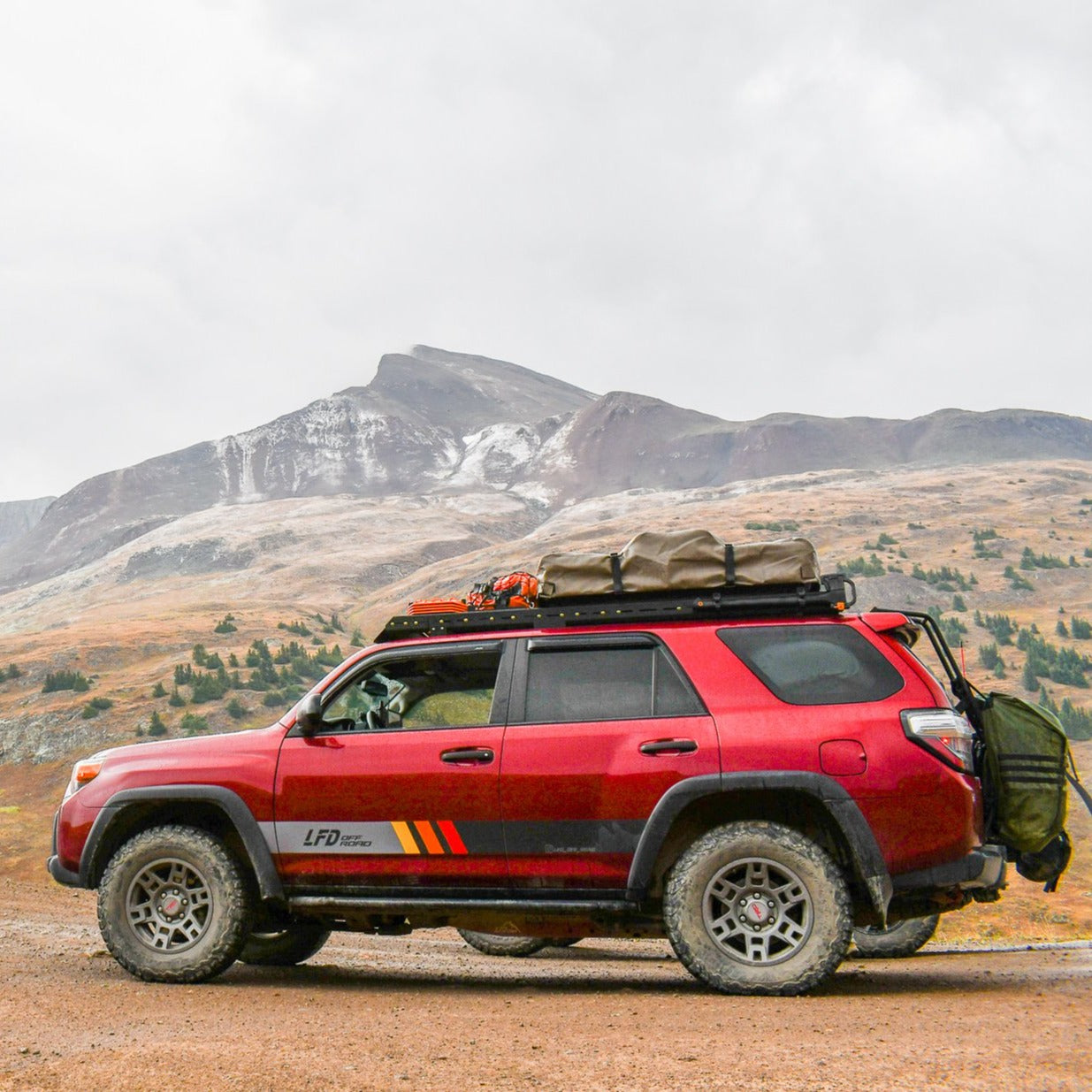 A red 5th Gen 4Runner with a full roof rack installed, set against a mountainous backdrop.