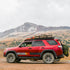 A red 5th Gen 4Runner with a full roof rack installed, set against a mountainous backdrop.