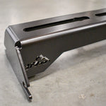 A black metal crossbar designed to be mounted on factory roof rails of a vehicle, featuring multiple holes for accessory mounting.