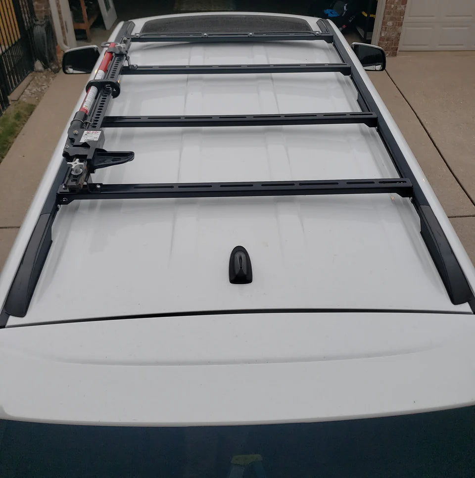 Ruggedized Crossbars mounted on the roof of a vehicle, including integrated wind fairing and standard crossbars with a visible logo on the fairing.