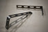 A pair of stainless steel universal awning mounts with multiple bolt holes, designed to be mounted on a vehicle roof rack.