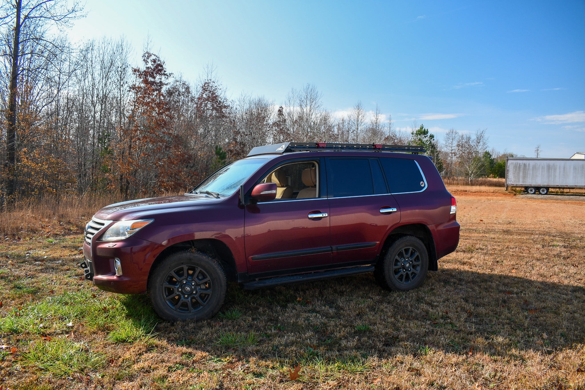 A red Land Cruiser 200 SUV with a full stainless steel roof rack installed on top.