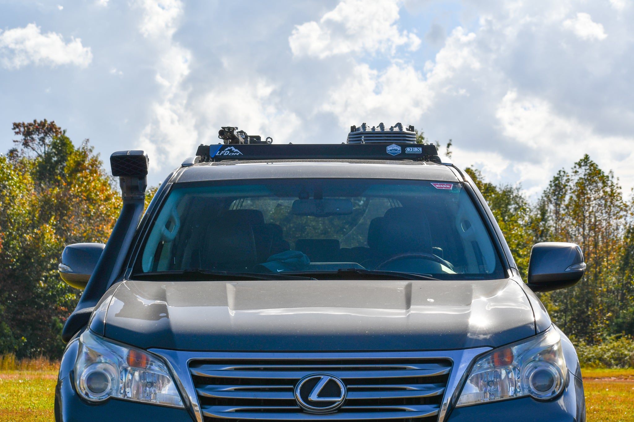 A silver Lexus GX460 SUV with a wind fairing installed on the roof rack.