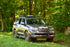 A GX460 SUV with the Ruggedized Crossbar Kit installed on the roof rails, set in a forested area.