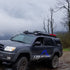 A black 4th Gen 4Runner with a roof rack featuring side rails and crossbars against a backdrop of a overcast sky and trees.