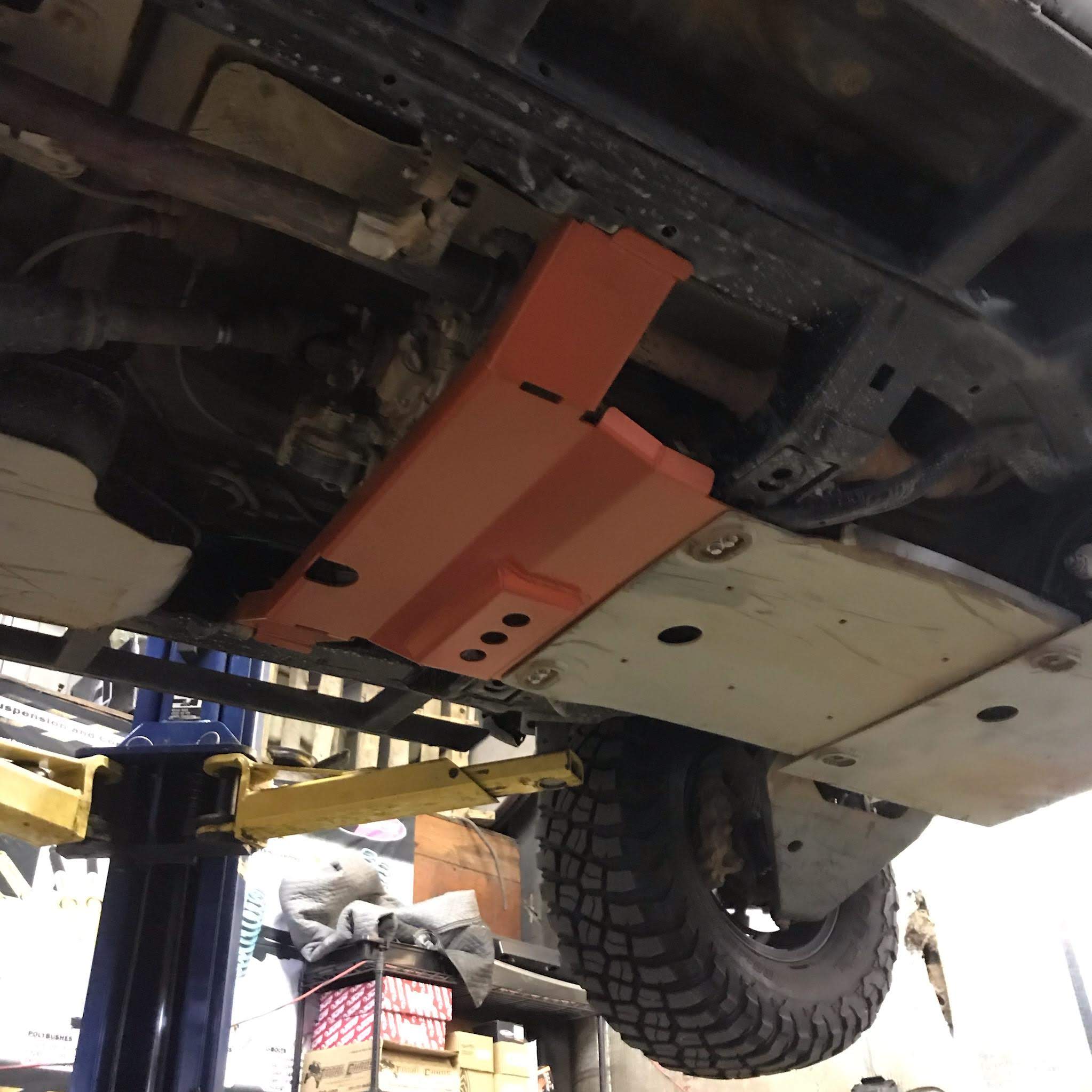 A red transfer skid plate installed underneath the rear section of a vehicle, in this case a 5th Gen 4Runner.