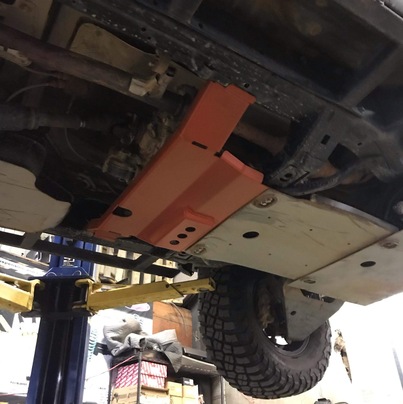 A red transfer skid plate installed underneath the rear section of a vehicle, in this case a 5th Gen 4Runner.