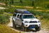 A white 2nd Gen Toyota Tacoma with a powder-coated black front bumper, driving on a dirt road.
