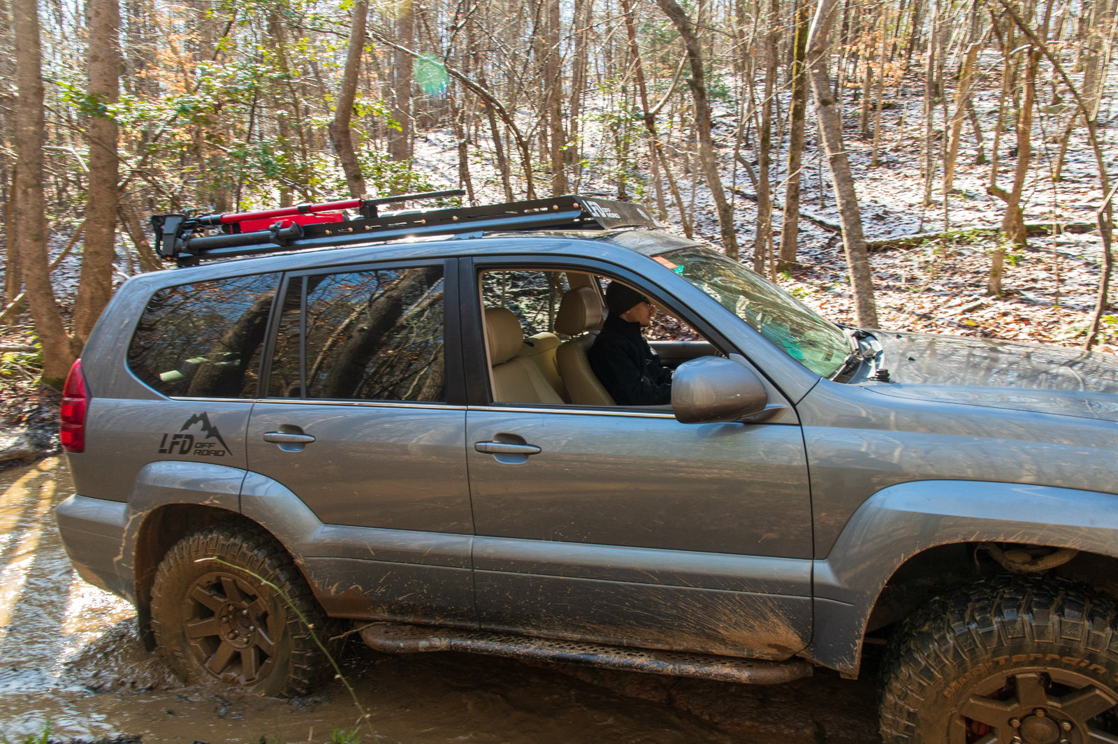 A GX470 Lexus SUV driving through a rugged terrain with rock sliders installed on the sides for protection.