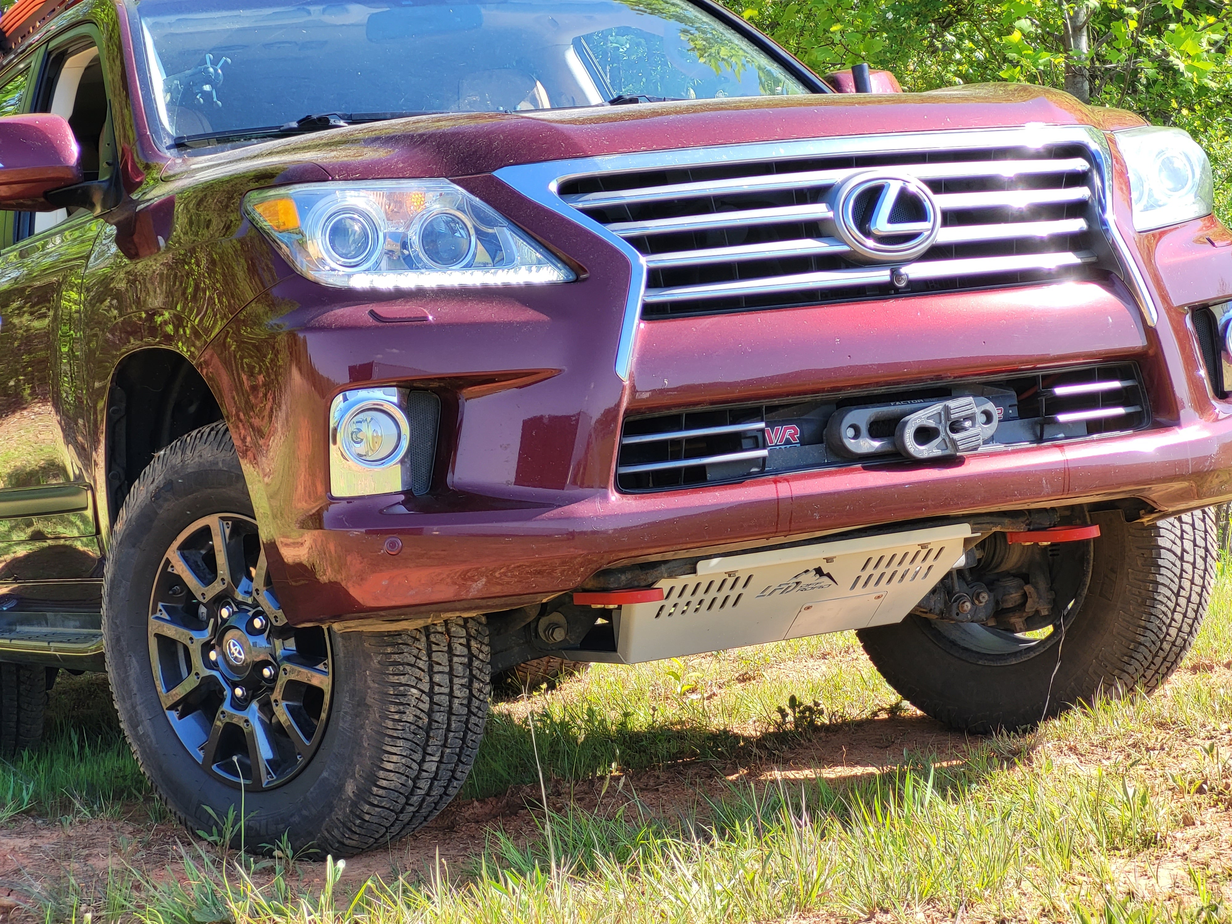 A front skid plate on a red Lexus LX570, showing the steel plate beneath the front bumper.