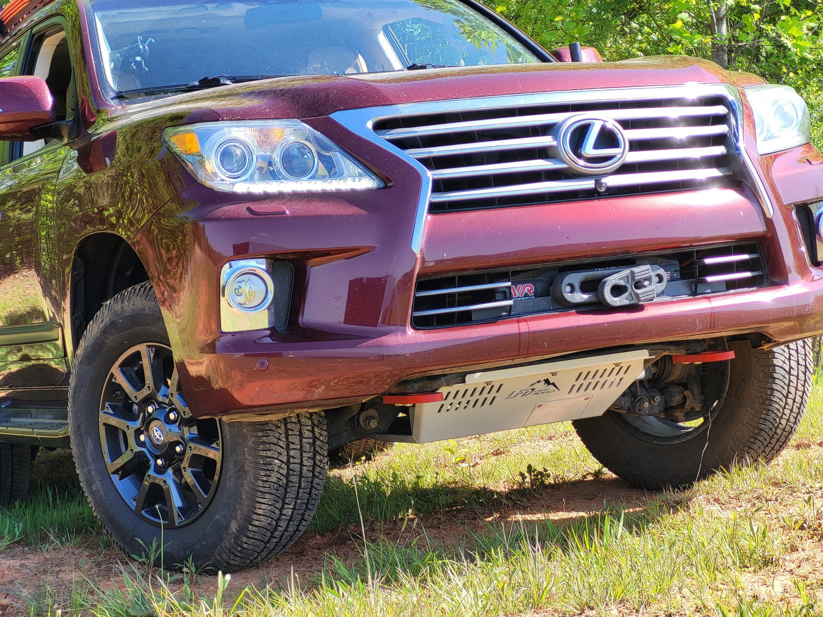 A front skid plate on a red Lexus LX570, showing the steel plate beneath the front bumper.