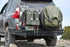 A dual jerry can mount attached to the rear bumper of a vehicle, with one canister partially visible and the other removed, revealing the mounting mechanism.