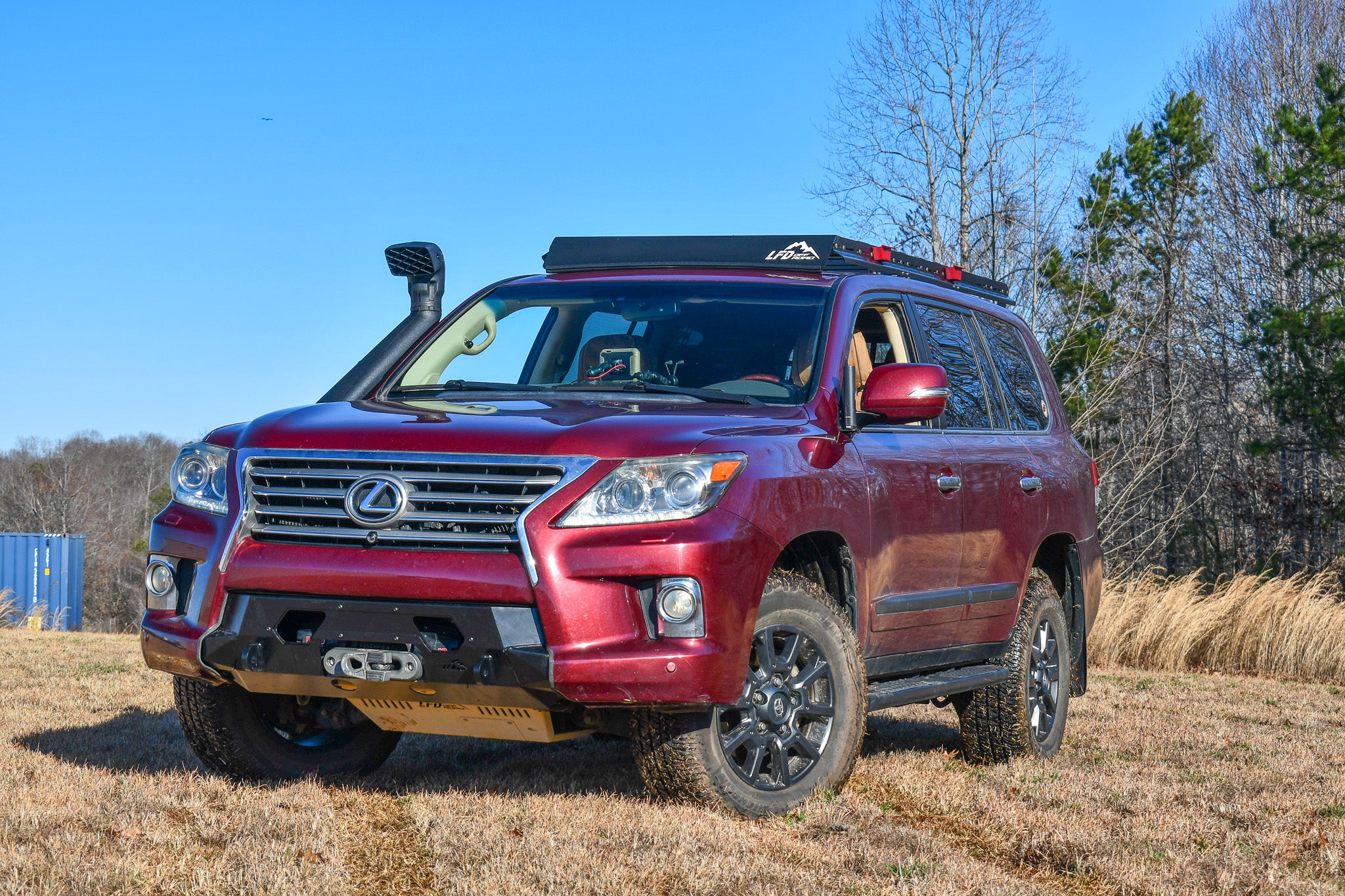 A red Lexus LX570 with the new front bumper installed, featuring a winch and recovery points, positioned in a natural outdoor setting.