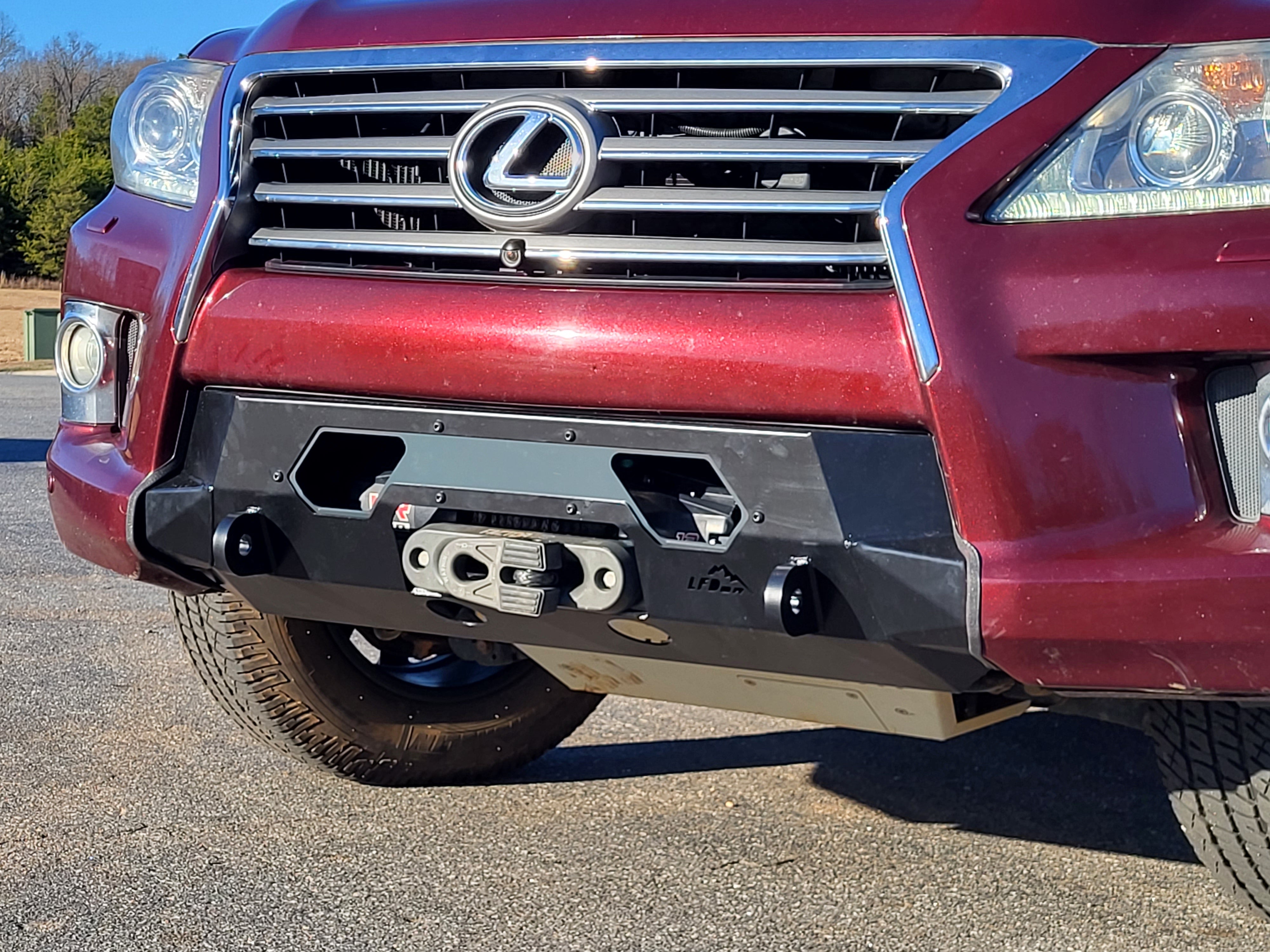 A red Lexus LX570 with the new front bumper installed, featuring a winch and recovery points, positioned in a natural outdoor setting.